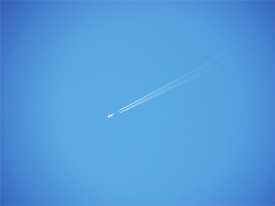 空を飛ぶ飛行機と、縦に二つ伸びる飛行機雲