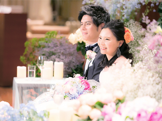 結婚式で花に囲まれた高砂に座る新郎と山下弘子さん