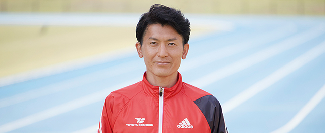 陸上競技場を背景に正面を向いている糟谷悟さん
